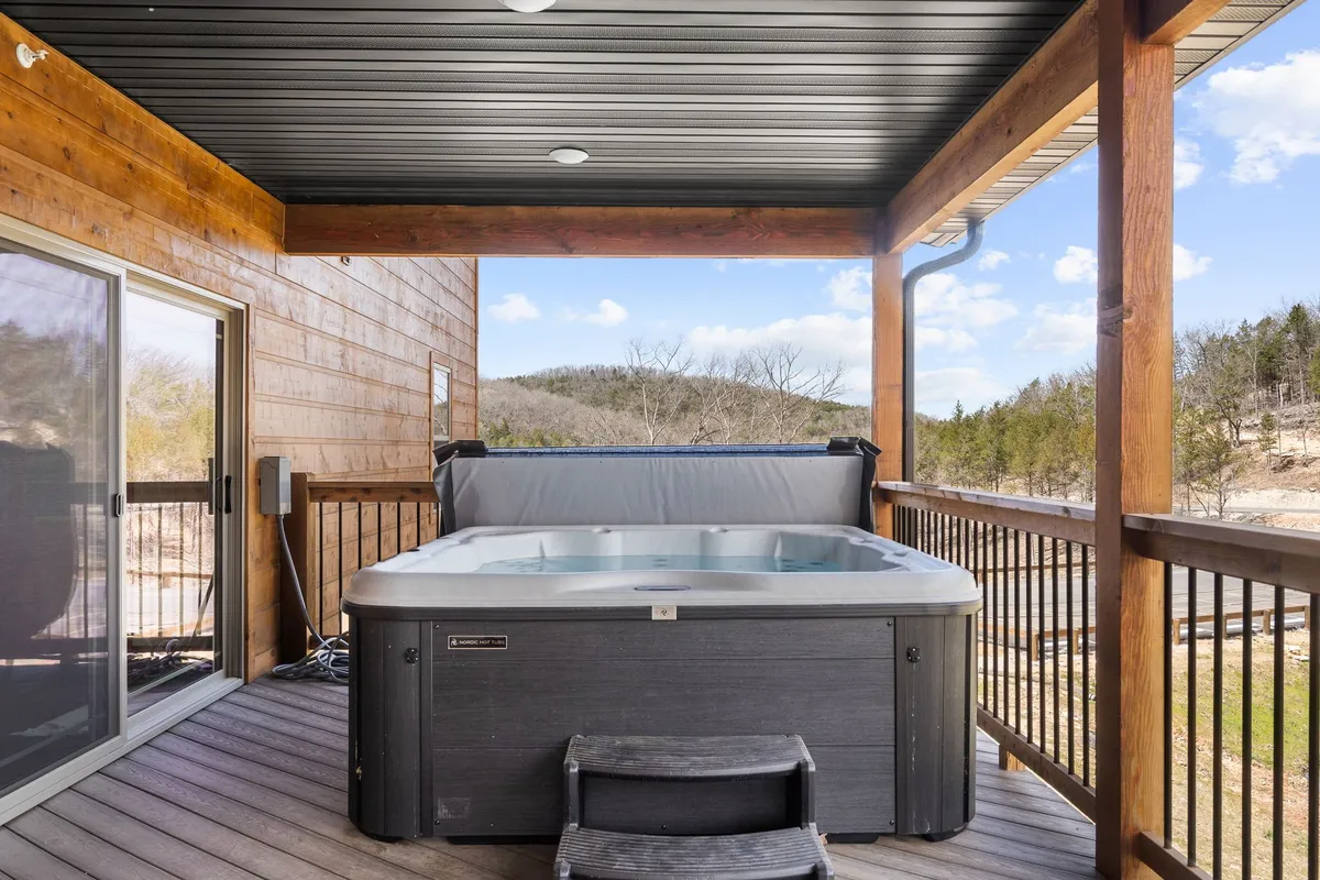 An inviting wooden deck with a hot tub sits framed by a tranquil mountain view. The hot tub is the focal point, with the deck seamlessly merging into the natural landscape, offering a breathtaking vista for stargazing or watching sunsets. The scene exemplifies peaceful privacy and relaxation in nature.