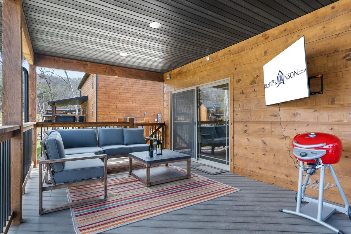A cozy outdoor seating area featuring a grill, a decorative rug, and a television, ideal for group barbecues, al fresco dining, or watching games together. The setting is casual yet inviting, emphasizing opportunities for shared activities and fun.