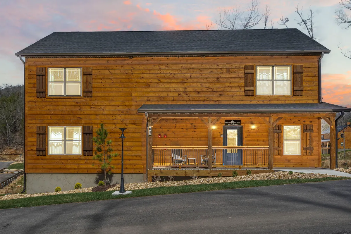 A welcoming exterior view of a brand-new wooden home with a spacious front porch, large windows, and fresh landscaping. The porch is set up for outdoor relaxation, and the newness of the construction is clearly visible.