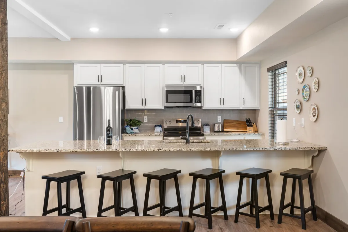 A bright kitchen featuring a granite countertop, stainless steel appliances, and a row of bar stools at an island—inviting guests to gather, chat, or help with meal prep. The design encourages interaction and shared moments.