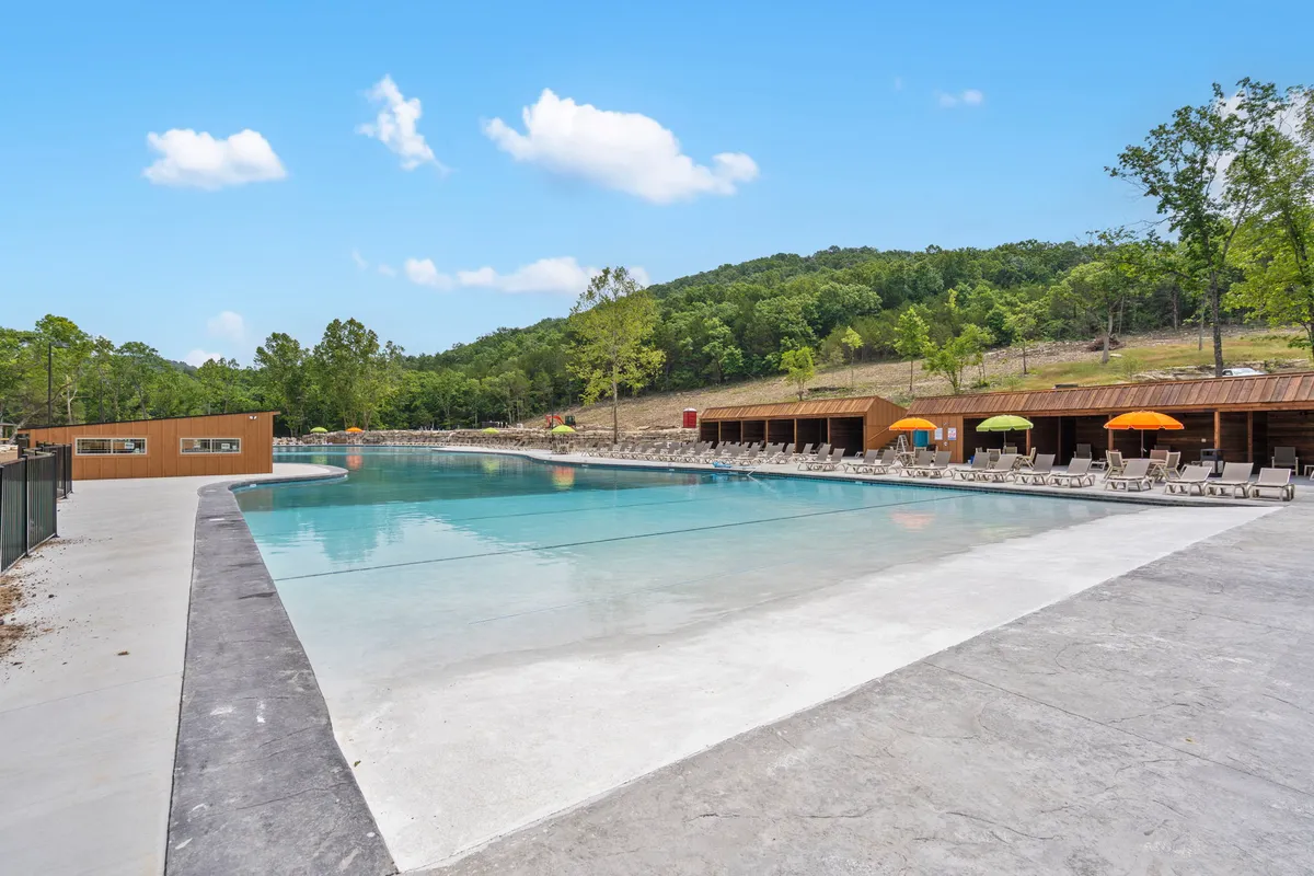 An inviting outdoor swimming pool area featuring lounge chairs, cabana structures, and rolling green hills in the background. The pool area is designed for social gatherings and summer relaxation, with views amplifying the seasonal enjoyment on offer.