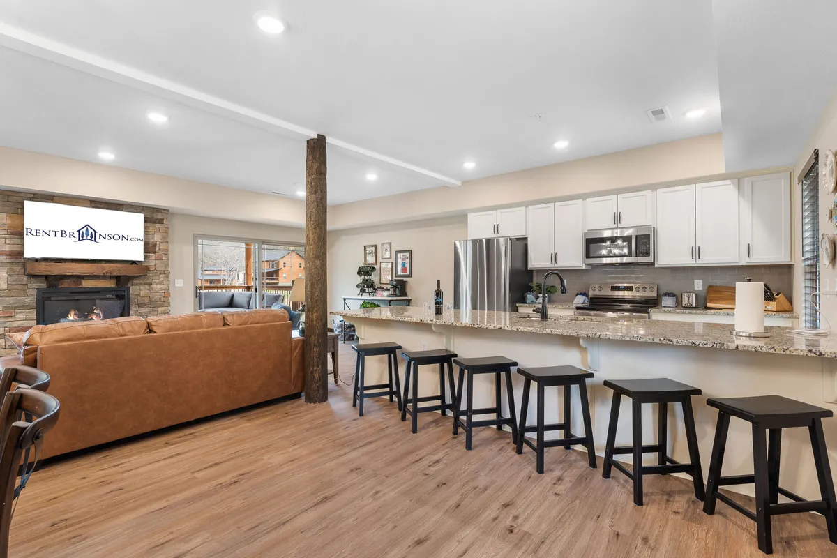 A broad shot showing an open living and kitchen space with a kitchen island, sofa, fireplace, and TV. This perspective emphasizes the fluidity between cooking, dining, and lounging zones, ideal for group gatherings and celebration.