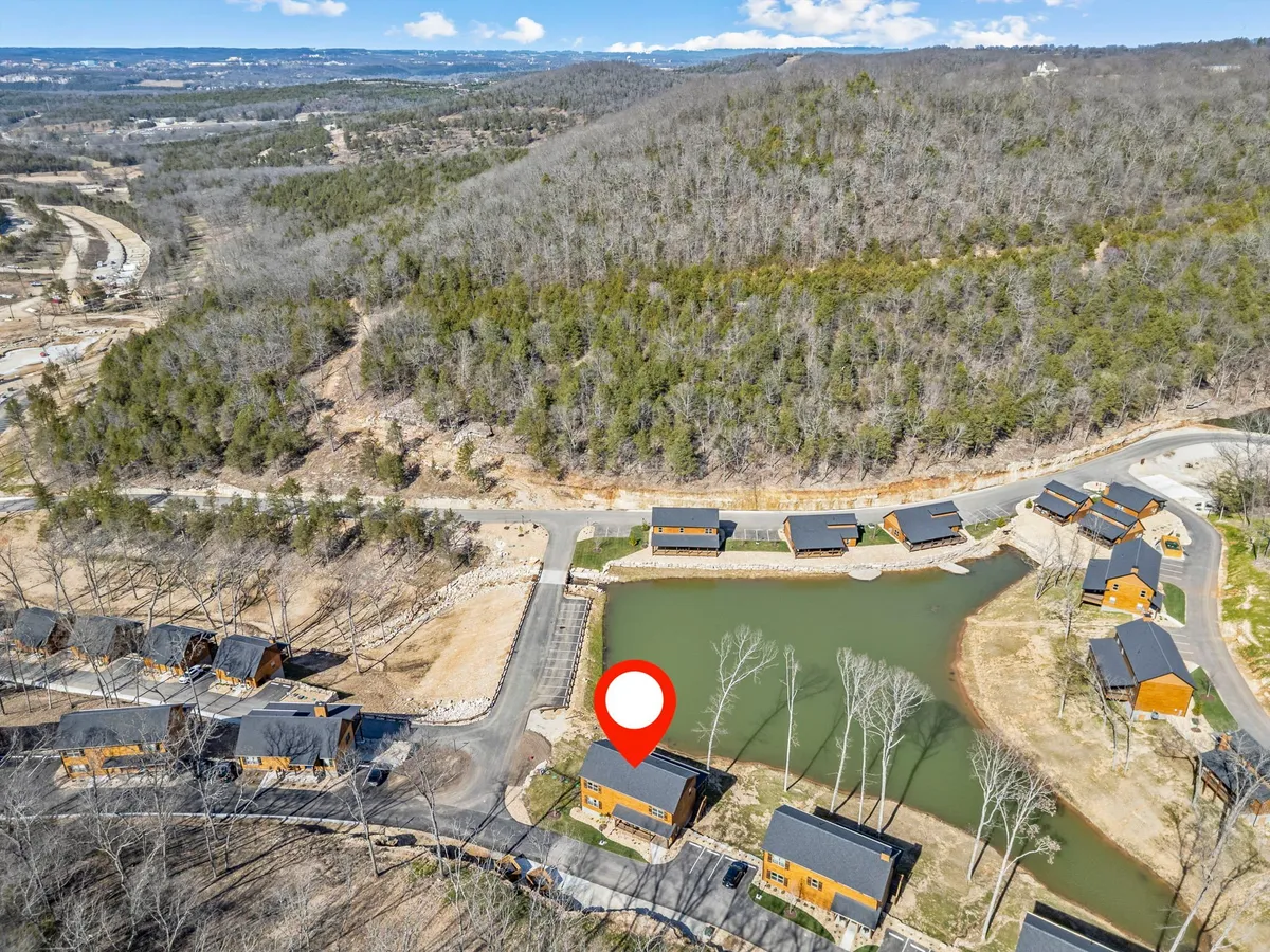 A tranquil scene featuring cozy cabins nestled beside a picturesque pond, surrounded by lush forest. The area is ideal for fishing, relaxing by the water, or enjoying the natural beauty of the camp. Winding pathways suggest easy access to outdoor activities and peaceful exploration.