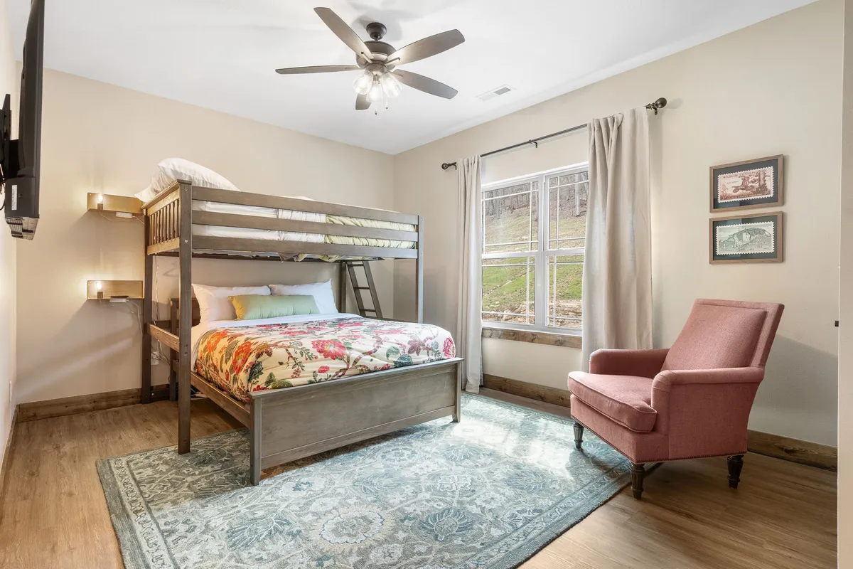 A family-friendly bedroom with a bunk bed and armchair positioned beside a window. The soft rug, warm tones, and playful setup create a welcoming setting ideal for children or larger groups looking for flexibility and comfort.