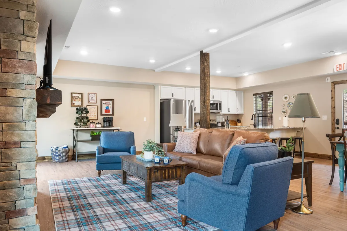 A warm, inviting living room with a central stone fireplace, plush sofas arranged for conversation, a coffee table, and decorative wall art. The space radiates comfort and is perfectly suited for social gatherings, game nights, or relaxing by the fire.