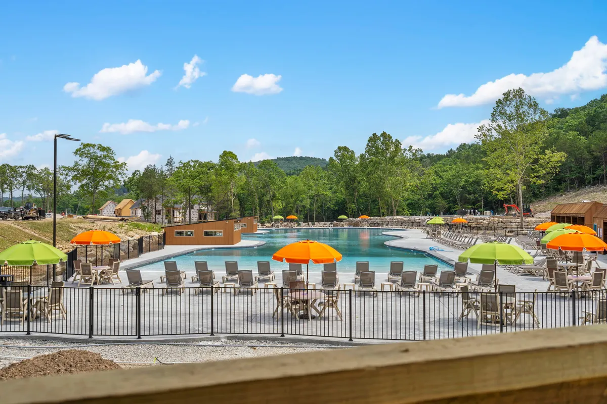 An exterior shot of the community’s outdoor pool, surrounded by colorful umbrellas, lounge chairs, and lush greenery. The scene is cheerful, showing people swimming, sunbathing, and socializing in a lively, inviting atmosphere.