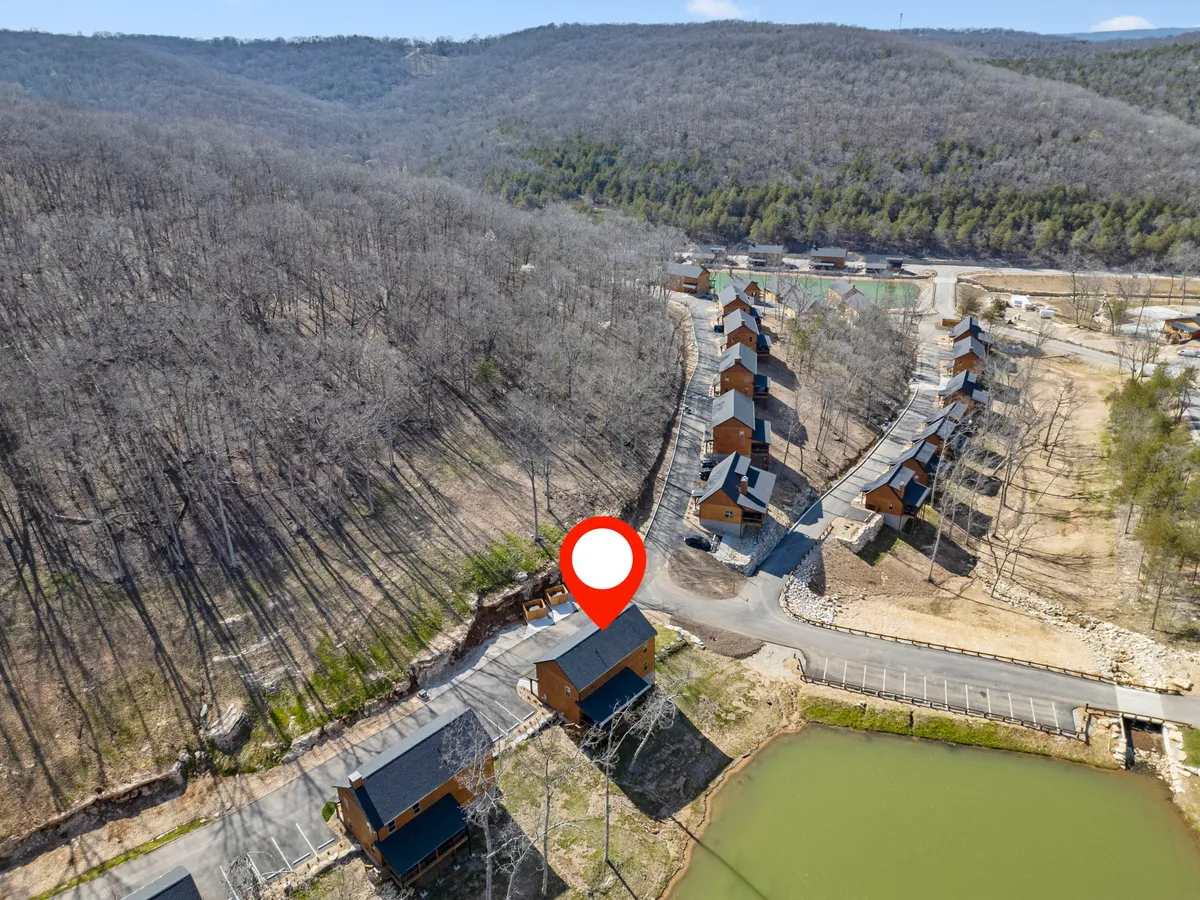 A broad exterior perspective showing wooden cabins by a lake, with surrounding mountains and wooded areas. The scene conveys serenity and a strong connection to nature, inviting extended exploration of the landscape.