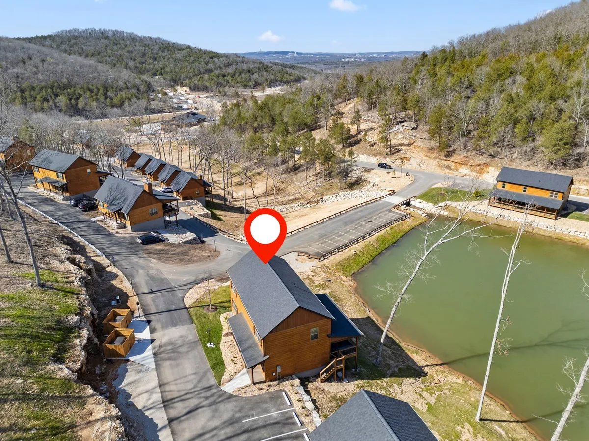 A peaceful exterior shot featuring cabins beside a pond, surrounded by lush trees. The pond is close to the accommodations, capturing the allure of fishing, sunset watching, and spending time by the water. The expansive outdoor environment highlights the harmony between living spaces and nature.