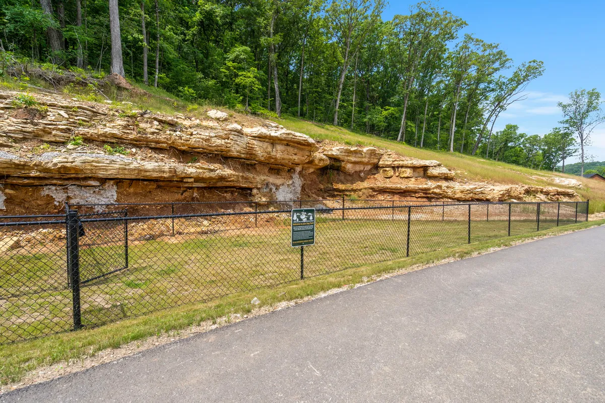 An exterior shot centered on a distinctive rock formation with signage nearby and a fenced area, suggesting accessible trails and natural features ready to be explored. The area is surrounded by greenery, making it ideal for walks and outdoor discovery.